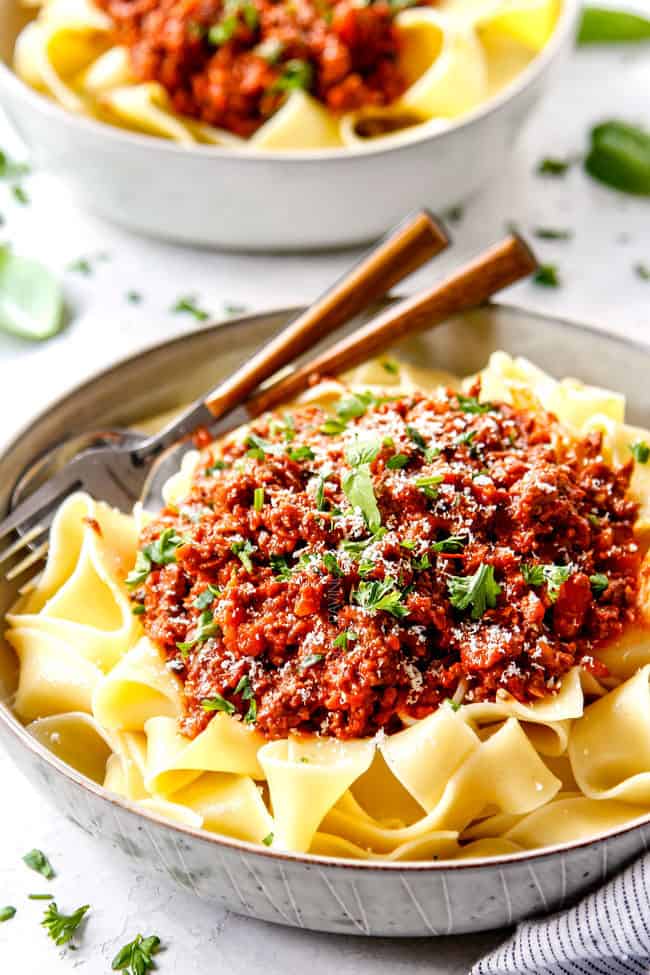 showing how to serve  best Bolognese recipe by adding sauce to pasta and topping with freshly grated Parmesan
