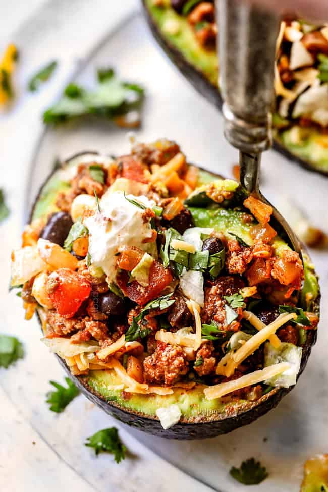 a fork taking a bite of  stuffed avocados 