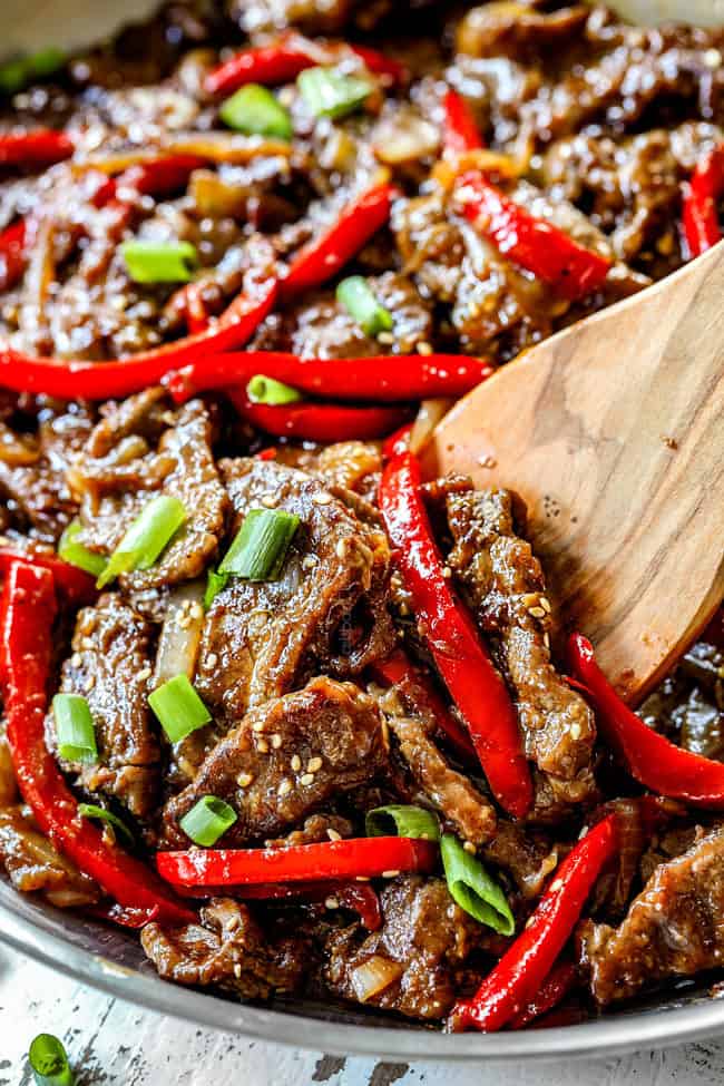 showing how to make Szechuan Beef by garnishing with green onions and sesame seeds