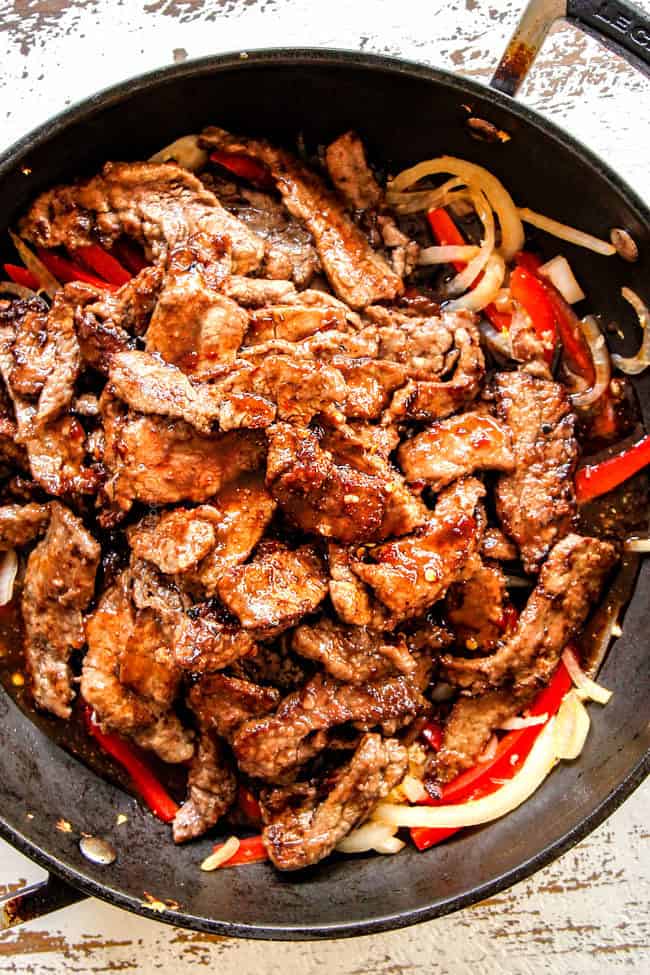 showing how to make Szechuan Beef by adding cooked beef Szechuan sauce to bell peppers and onions in a wok