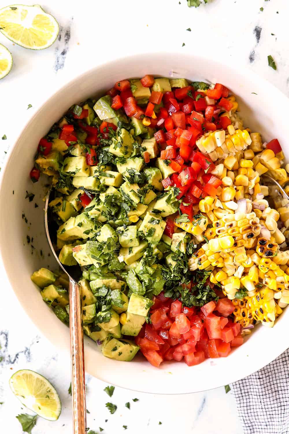 showing how to make avocado corn salsa by tossing avocados, corn, tomatoes, cilantro, red onions and cilantro together in a bowl with lime juice