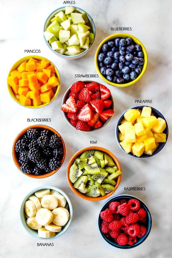 showing how to make acai bowls with bowls of fruit toppings: pineapple, apples, blueberries, strawberries, mangos, pineapple, kiwis, raspberries, blackberries