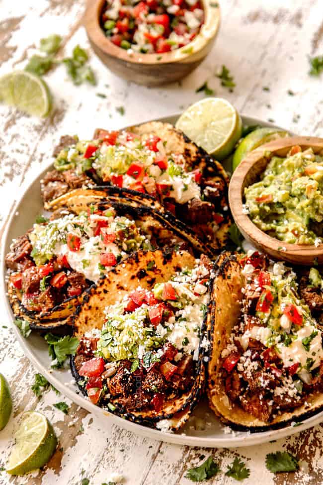 showing how to serve carne aada by adding to street tacos lined up on a plate in corn tortillas