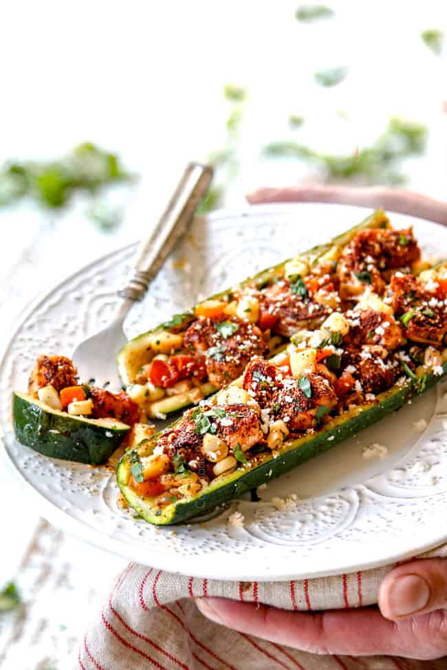 two hands holding a plate of zucchini boat recipe