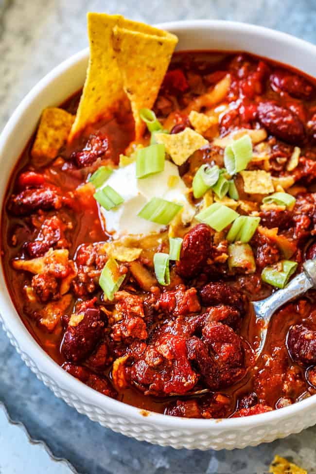a white bowl full of best crockpot chili recipe with a spoon taking a bite