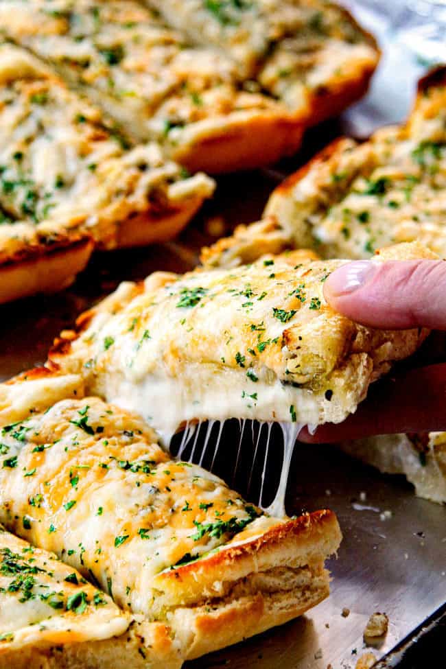 a hand taking a slice of cheesy garlic bread