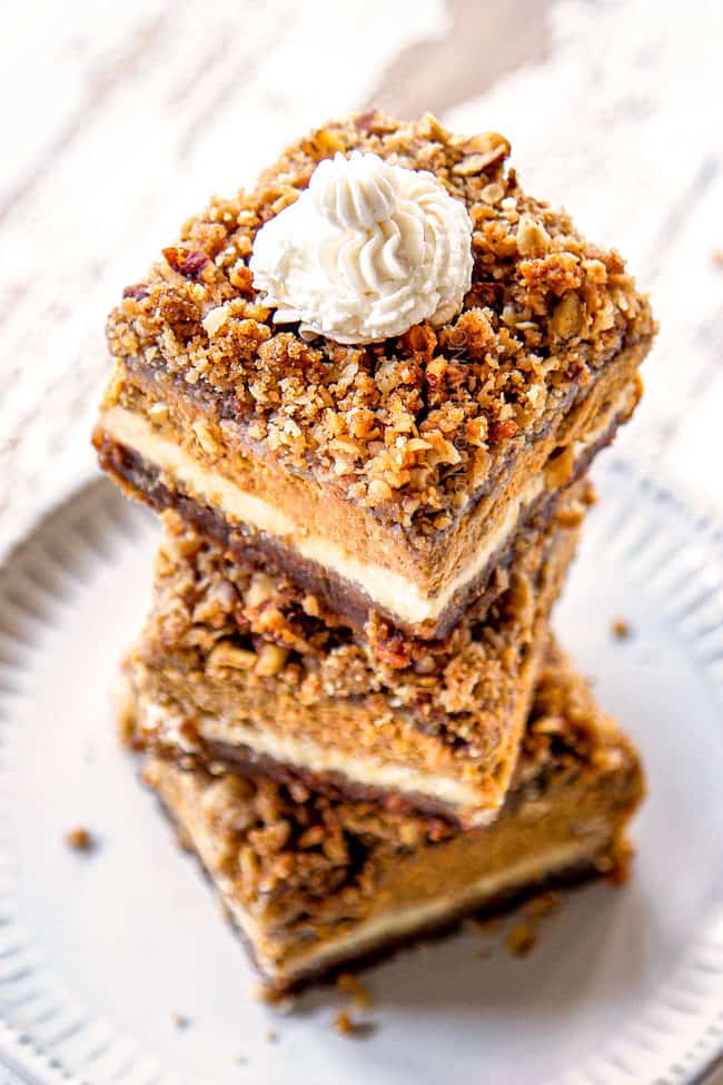 a tower of pumpkin cheesecake bars with streusel topping and whipped cream