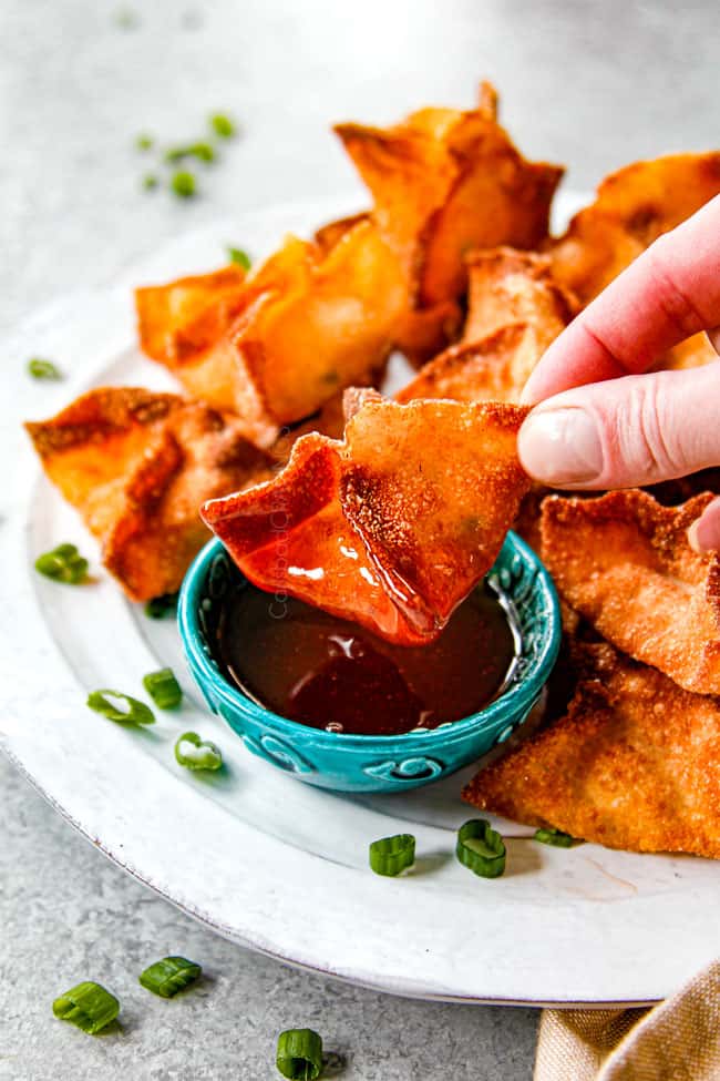 showing how to serve homemade crab wontons by dipping a rangoon into dipping sauce
