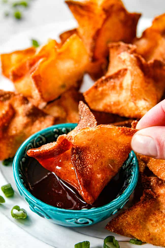 up close of dipping fried crab rangoon into sweet and sour sauce