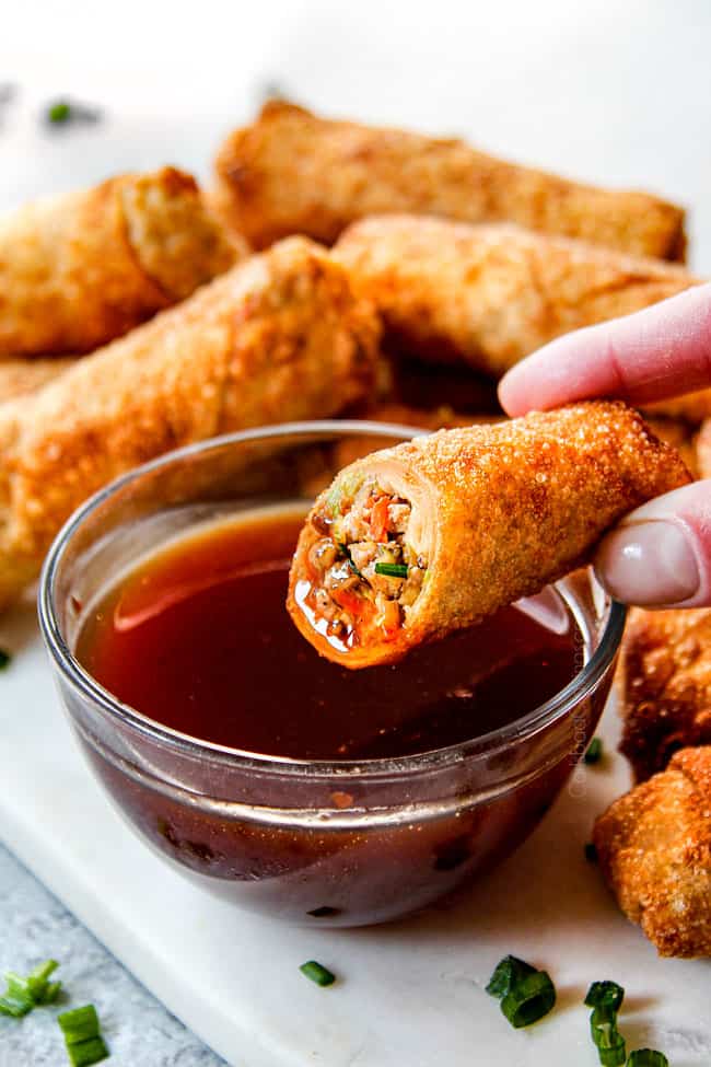 showing how to eat  pork egg rolls by dipping into dipping sauce