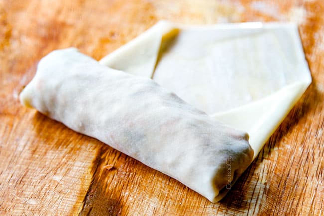 showing how to make pork egg rolls by rolling up wrapper until tight while squeezing out air