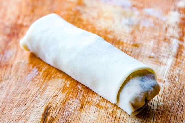 showing how to make egg rolls by rolling egg roll tightly up until completely sealed