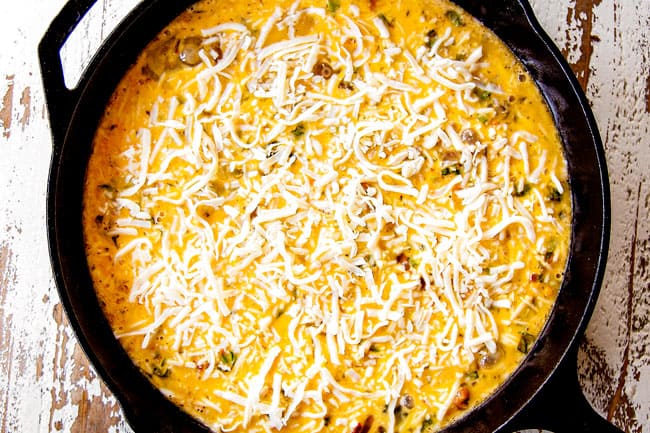 showing how to make frittata recipe by pouring egg mixture over vegetables and layering with cheese in a cast iron skillet.