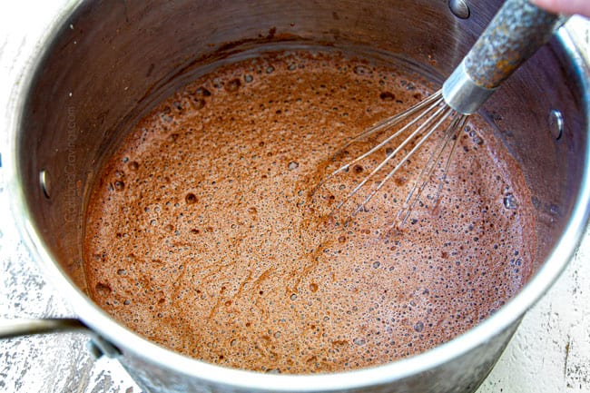 showing how to make homemade hot chocolate recipe by whisking in cocoa powder, sugar, milk and heavy cream