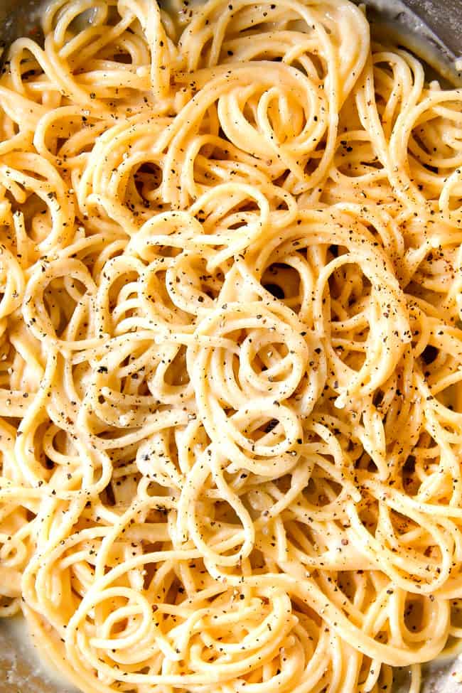 top view showing how to make cacio e pepe recipe by adding freshly cracked pepper to spaghetti in a skillet