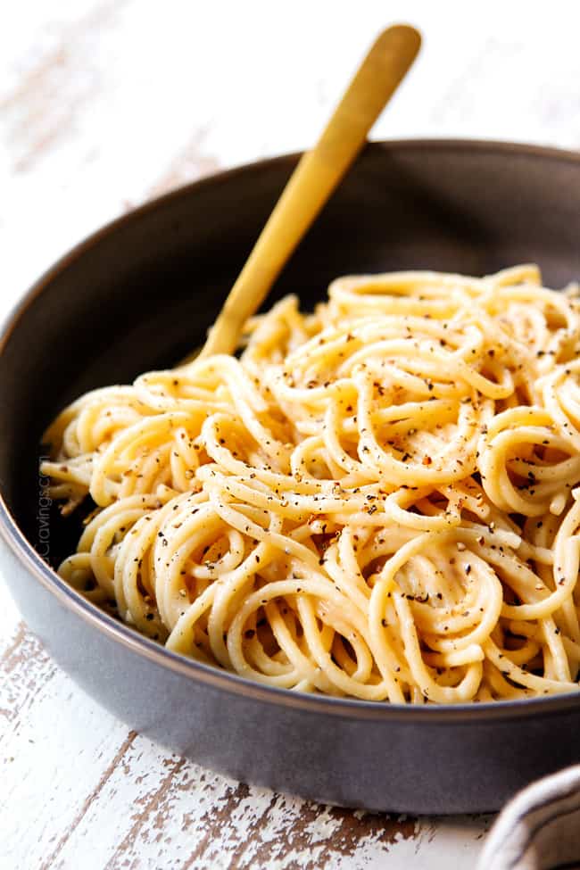 showing how to serve authentic cacio e pepe recipe by adding pasta to a bowl and garnishing with additional freshly cracked pepper and Pecorino Romano