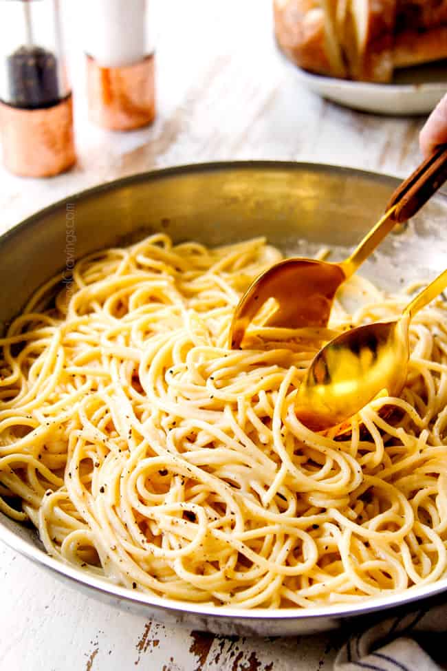 a pair of golden tongs picking up authentic cacio e pepe in a stainless steel skillet