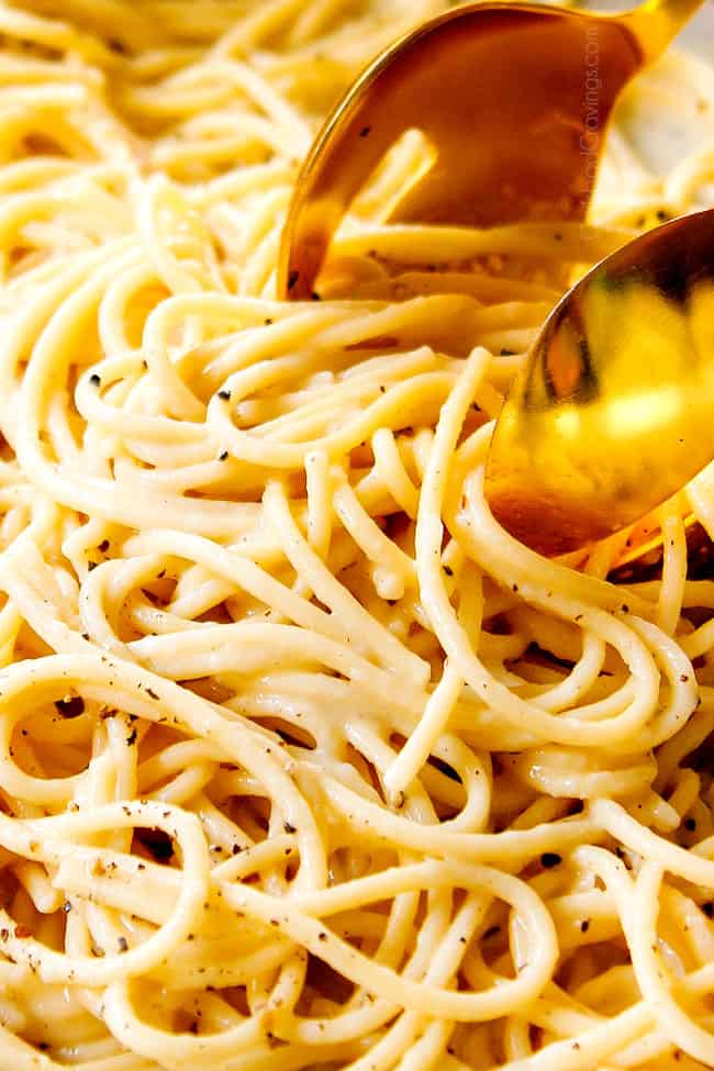 up close of serving cacio e pepe recipe by two golden tongs picking up the creamy pasta