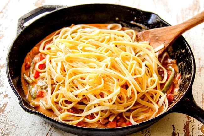 showing how to make Cajun shrimp pasta by adding pasta to cajun Alfredo sauce 