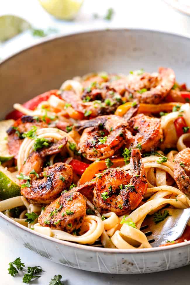 up close of a white bowl of Alfredo Cajun Shrimp Pasta recipe with shrimp, bell peppers, red onion, parsley and Parmesan
