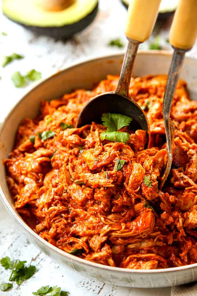 two tongs scooping up chicken tinga to serve