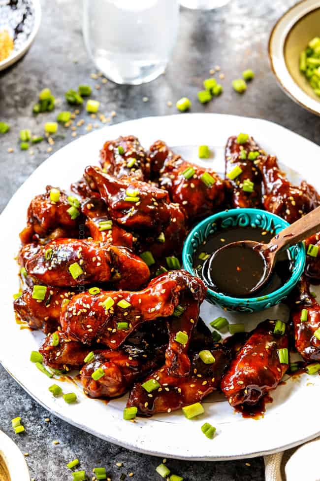 showing how to serve Korean Chicken Wings by adding  to a platter and garnishing with sesame seeds and green onions
