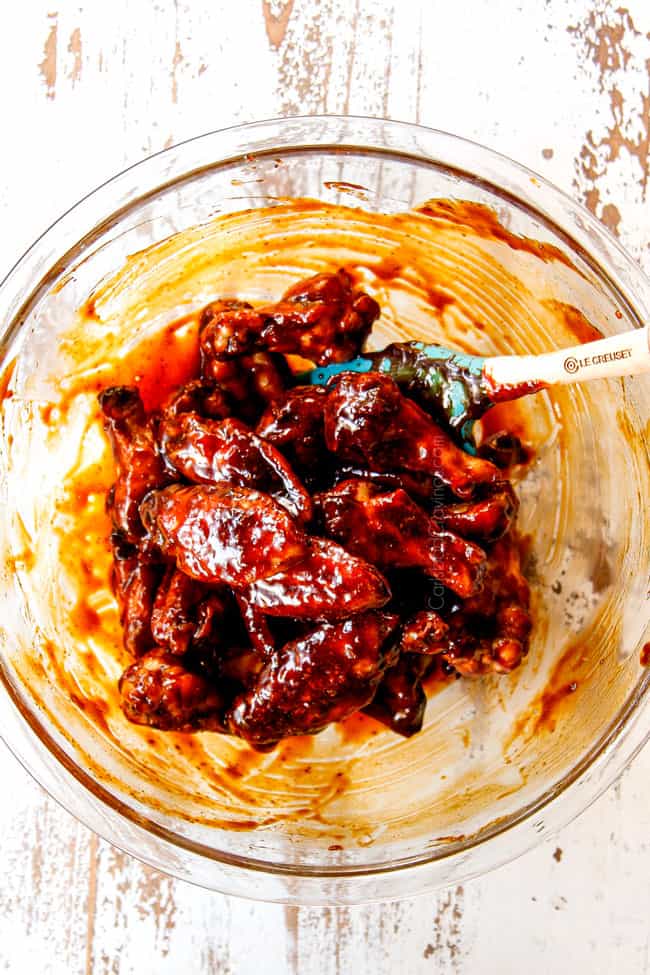 showing how to make Korean Chicken Wings recipe by stirring wings with Korean BBQ Sauce in a glass bowl with a spatula until coated 