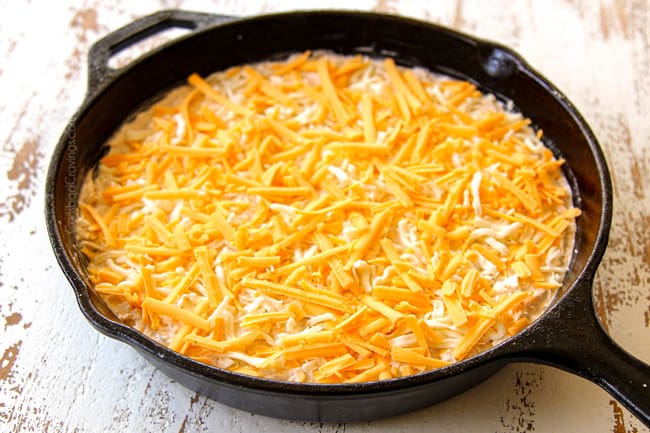 shwoing how to make crab dip by sprinkling the top with cheese