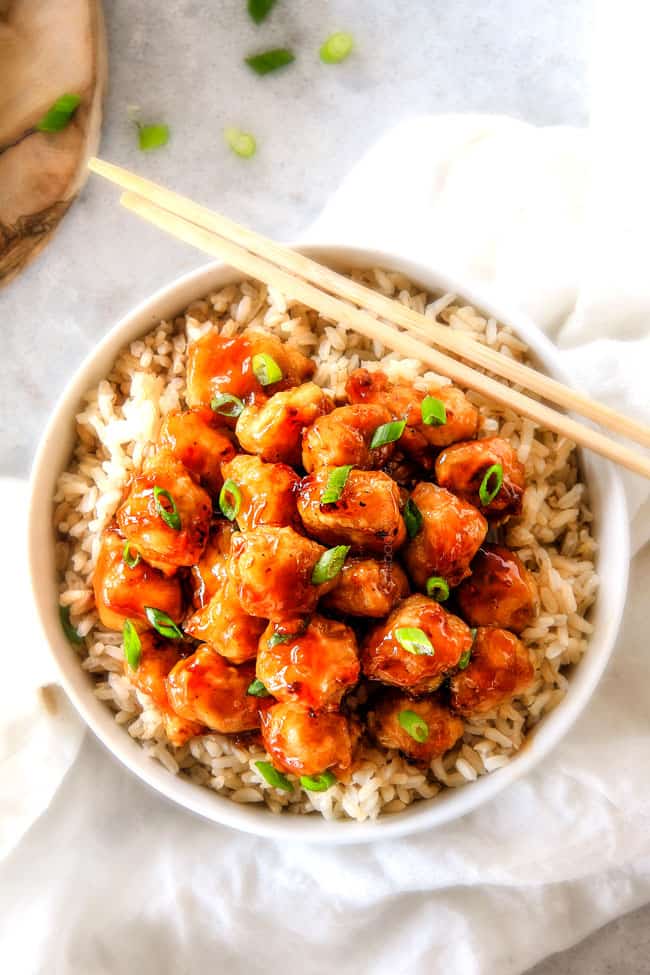 top view of a bowl of homemade orange chicken recipe served over rice with green onions and chopsticks 