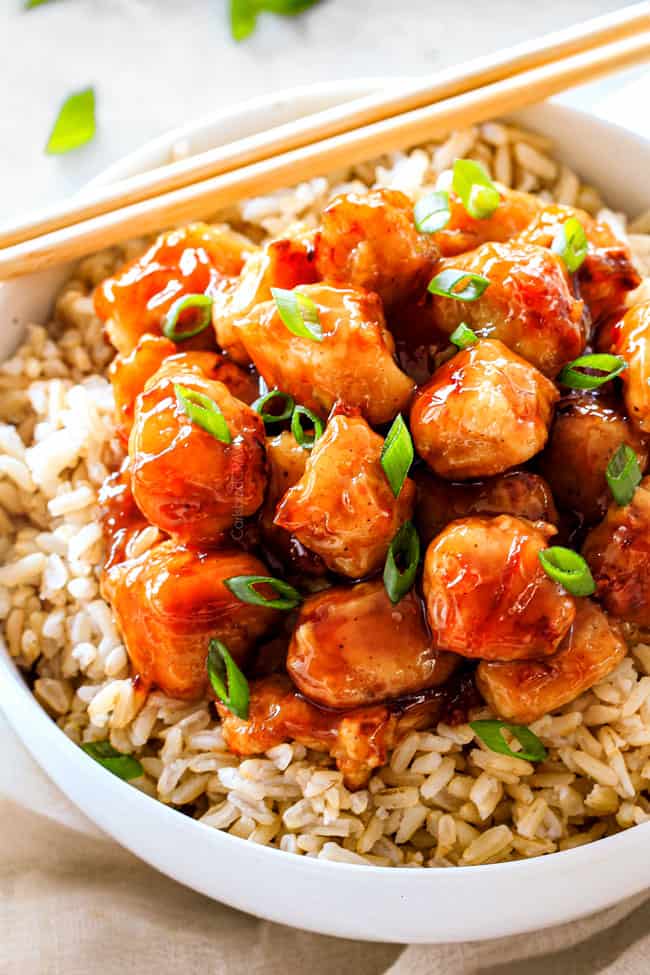 showing how to serve homemade orange chicken recipe by placing in a bowl with rice and garnishing with green onions