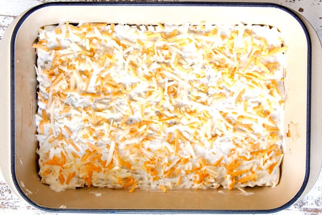 showing how to make Mexican Lasagna recipe by topping creamy layer with shredded cheese