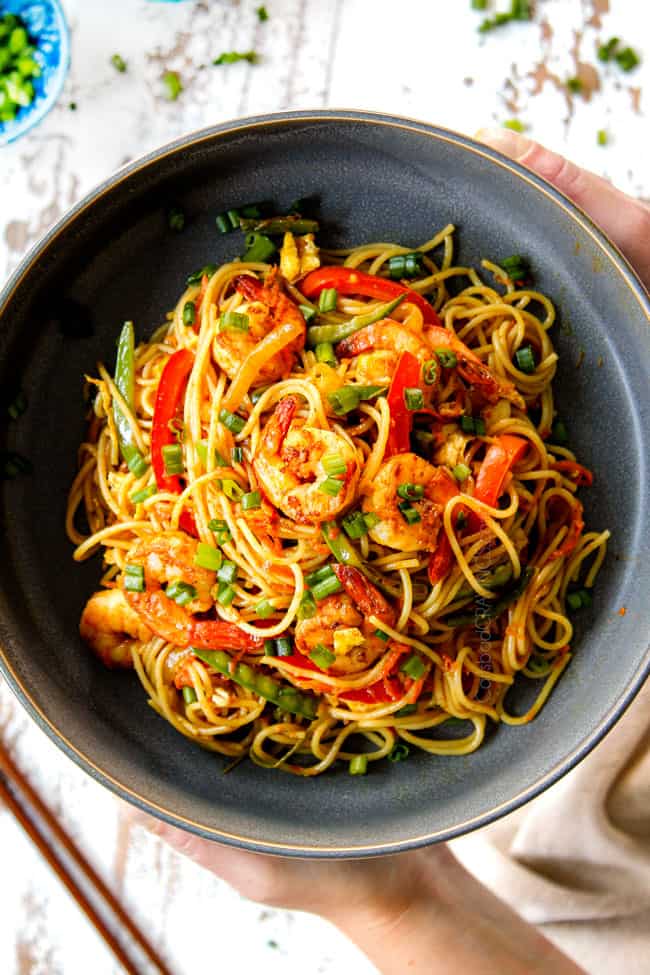 showing how to serve Singapore Noodles Recipe by adding to a bowl and garnishing with green onions