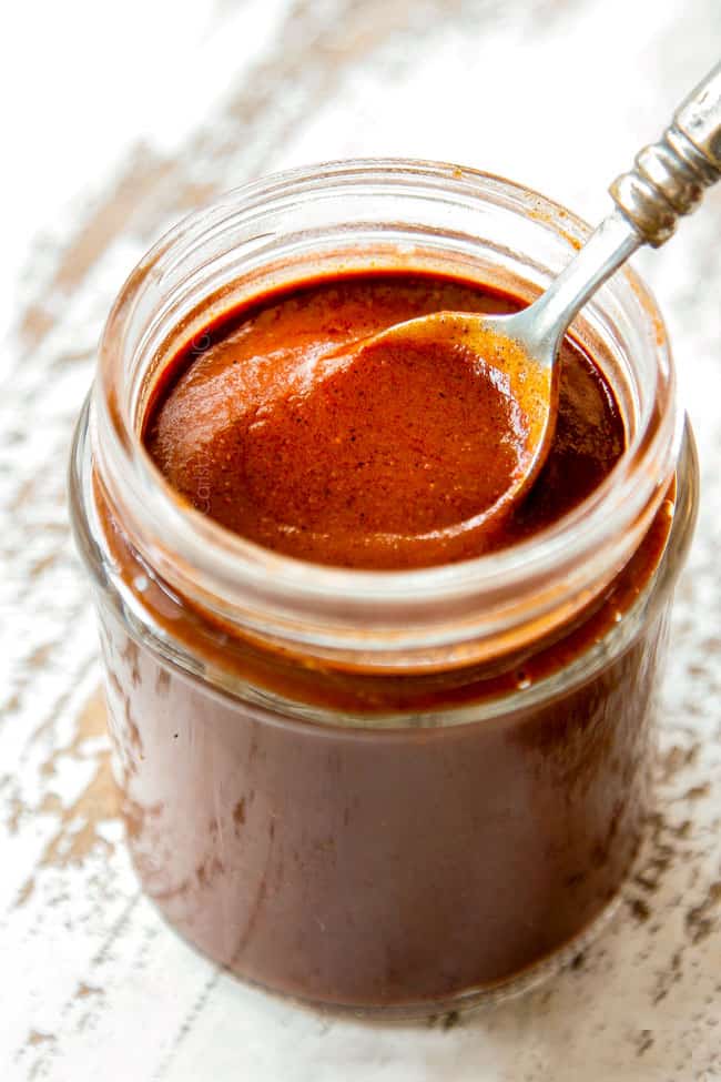 a spoon dipping into a jar of homemade enchilada sauce to show the consistency