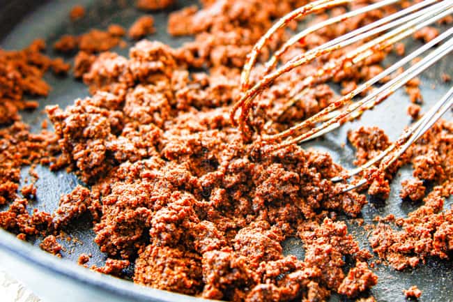 showing how to make enchilada sauce by whisking flour with oil and chili powder to create a roux in a cast iron skillet and bloom seasonings