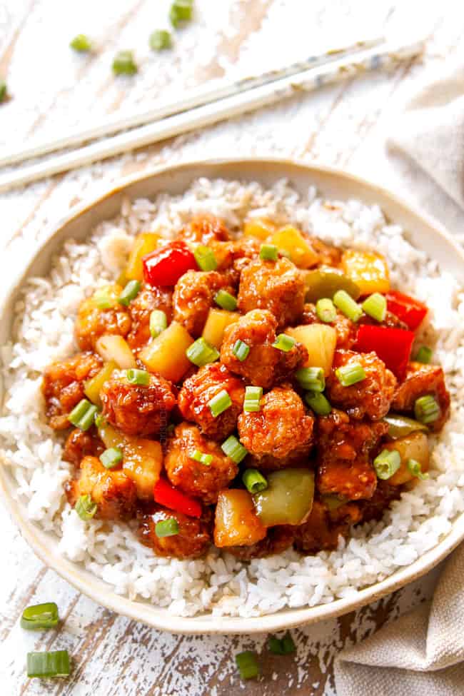 showing how to serve Sweet and Sour Chicken recipe by adding chicken to a bowl rice and garnishing with green onions