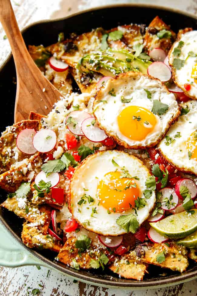 showing how to serve Chilaquiles Verdes by scooping up  chips and a fried egg with a wooden spoon