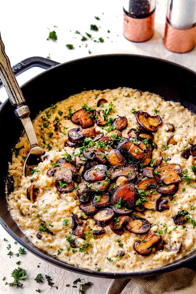 showing the correct consistency of easy mushroom risotto with a spoon in a black pot of risotto
