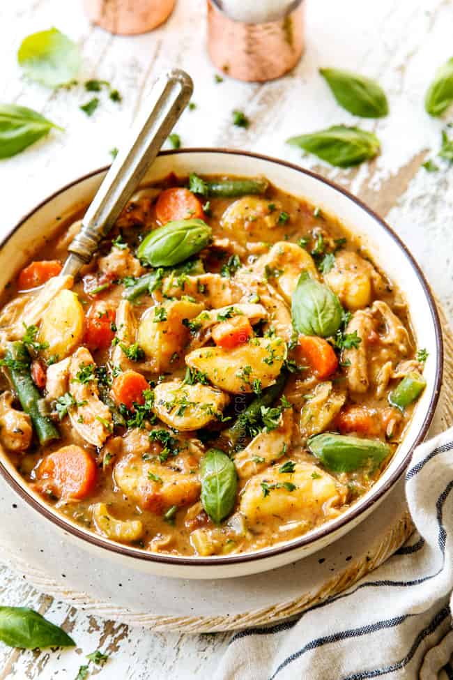 showing how to serve chicken stew by adding to a bowl and topping with fresh basil