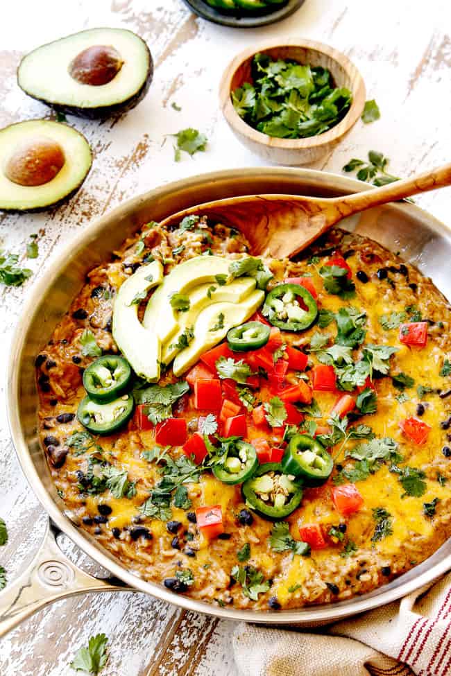 Green Chili Chicken recipe in a stainless steel skillet topped with tomatoes, jalapenos, cilantro and avocados