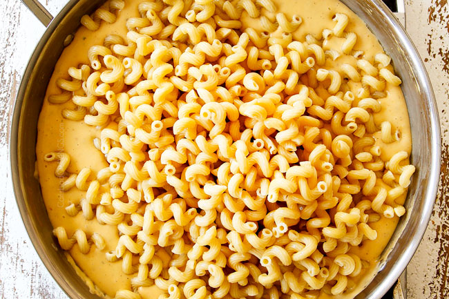 showing how to make mac and cheese by stirring pasta into cheese sauce