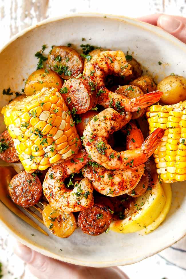 showing how to serve shrimp boil recipe by adding corn, shrimp, potatoes and sausage to  a plate and drizzling with lemon juice