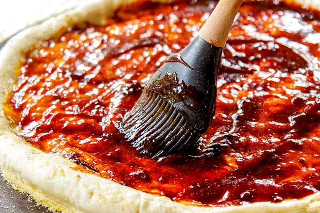 showing how to make BBQ Sauce over pizza doughQ Chicken Pizza recipe by cooking chicken in a cast iron skillet then tossing in BBQ sauce by spreading BB
