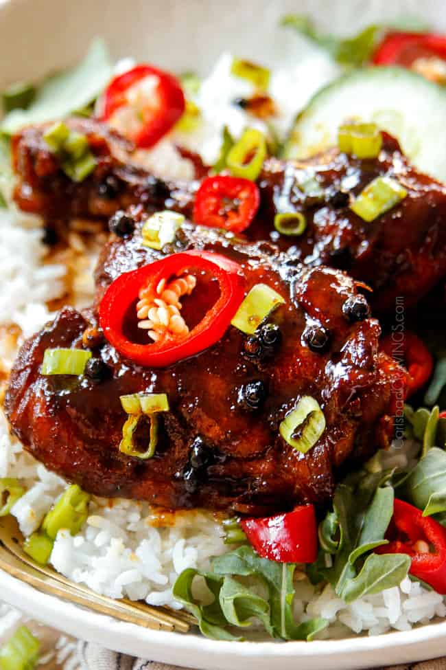 showing how juicy the Filipino Chicken Adobo recipe is with an up close view of bone-in chicken thigh coated in glaze and garnished with green onions served over rice in a white bowl
