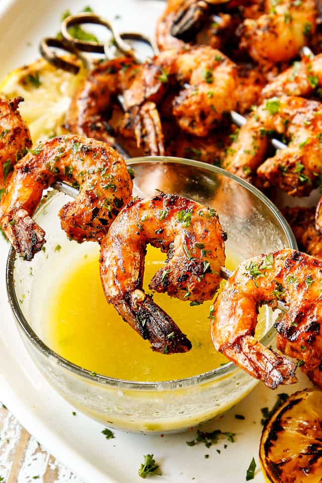 showing how to serve grilled shrimp skewers by placing skewer on a bowl of melted butter  to dip in