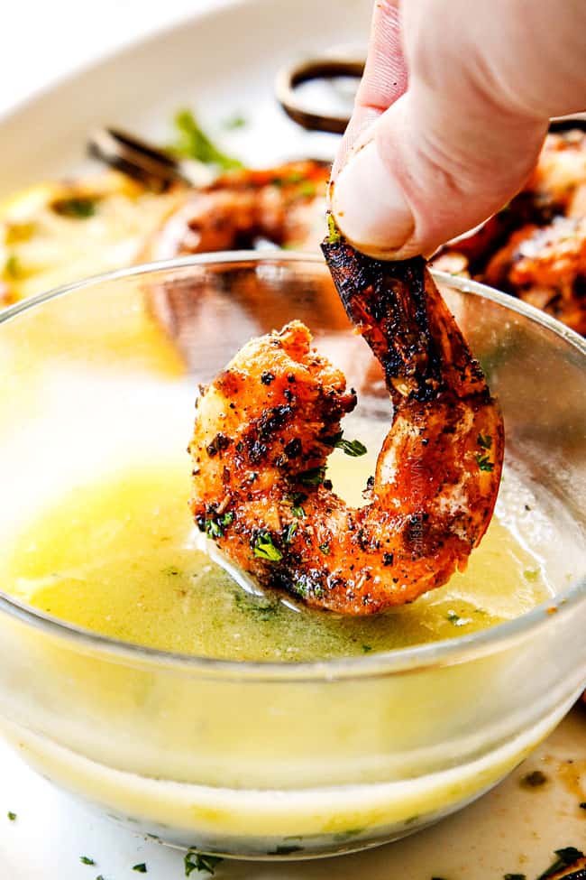 showing how to serve grilled shrimp recipe by dipping a piece of shrimp into lemon butter