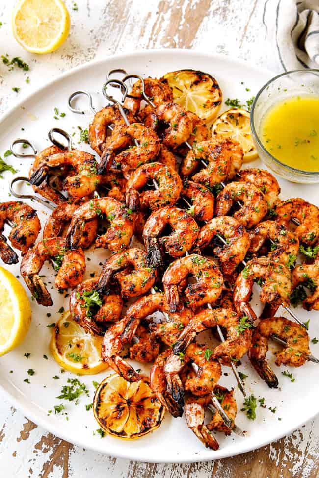 showing how to garnish shrimp recipe by stacking grilled shrimp skewers on a white plate and garnishing with parsley and lemon slices