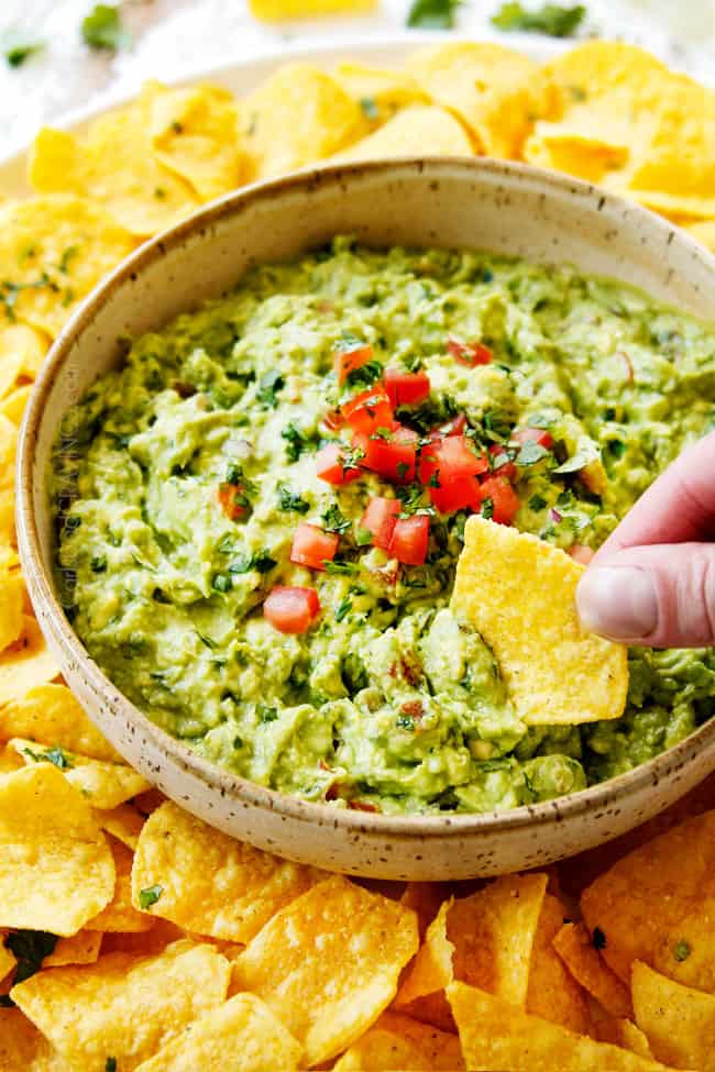 showing how to make best guacamole recipe by tasting guacamole with a tortilla chip