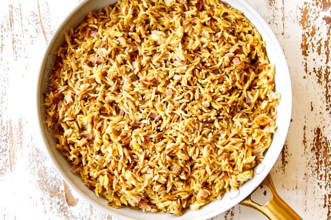 showing how to make Greek orzo pasta by cooking orzo with lemon juice and chicken broth in a white nonstick skillet