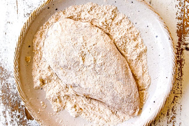 showing how to make coconut chicken recipe by dredging chicken in a shallow bowl of flour