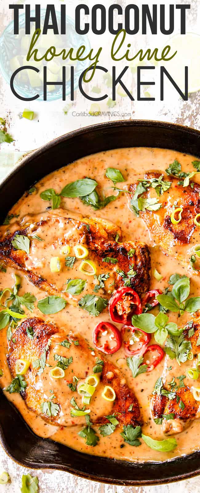 top view of coconut chicken recipe in a cast iron skillet garnished with red chilies, basil and cilantro